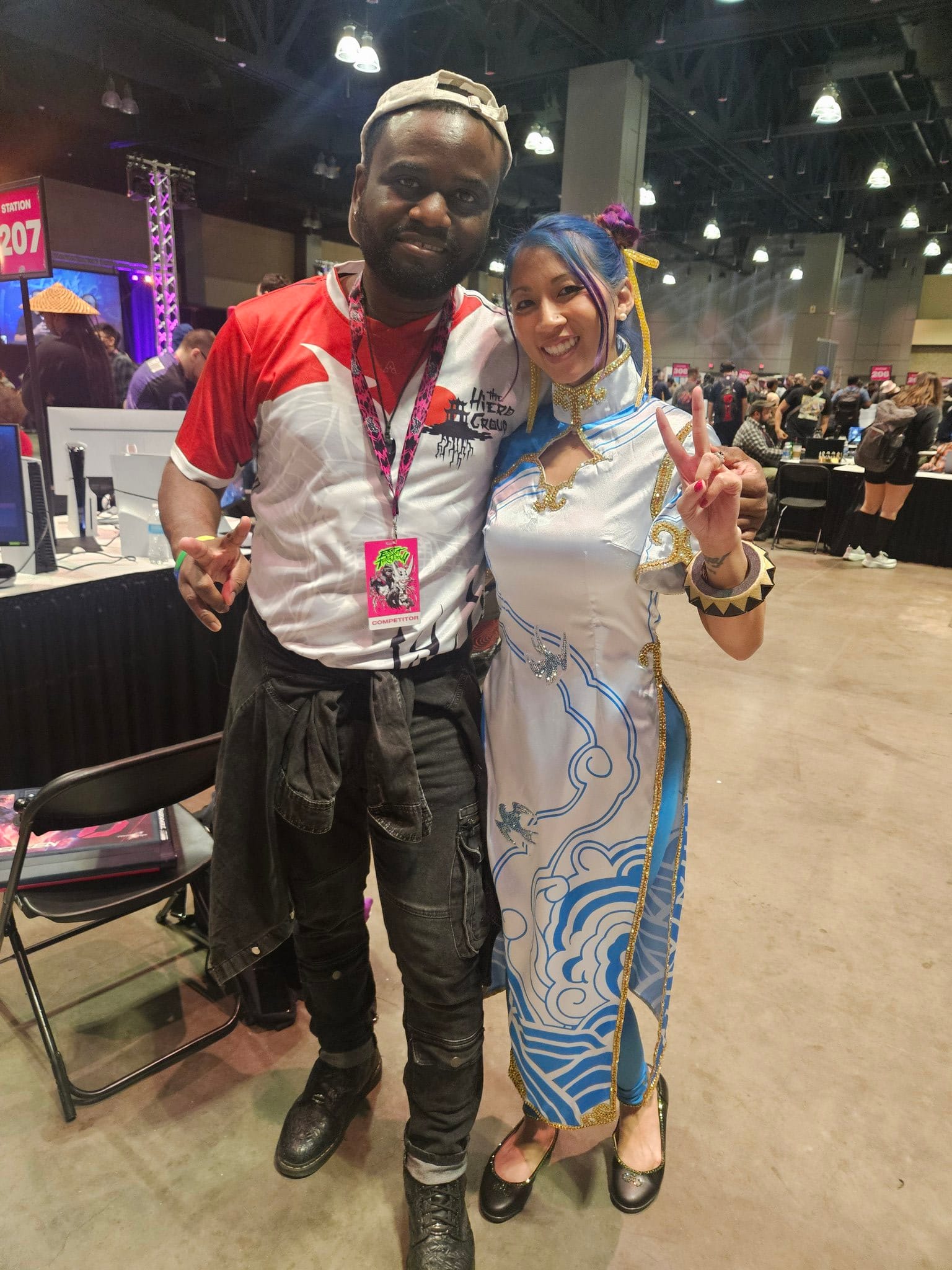 Ludovic Mbock, an African male wearing a esports jersey at a fighting game tournament, stands next to a Chun-Li cosplayer holding up the peace sign.