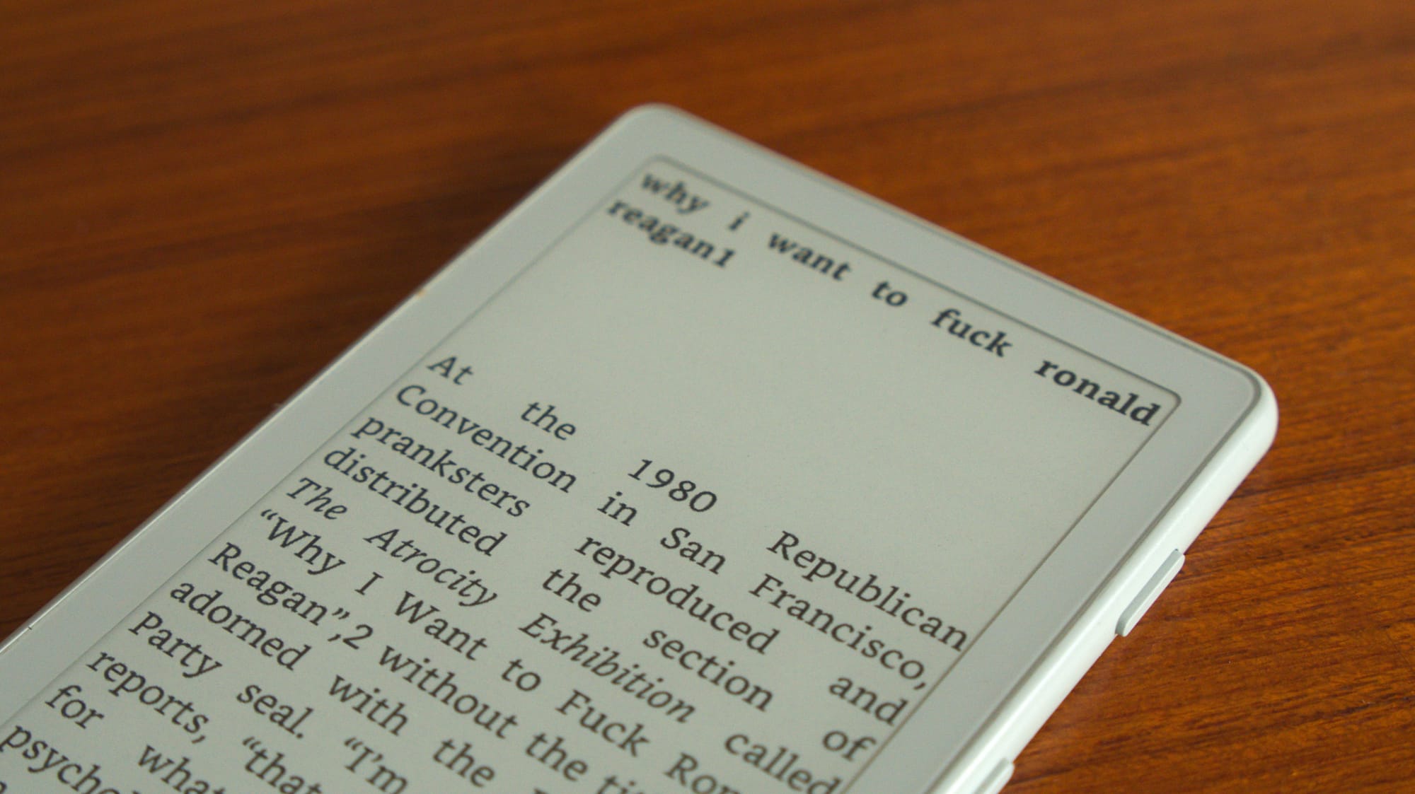Mark Fisher's blog analyzing the essay "Why I Want To Fuck Ronald Reagan" from The Atrocity Exhibition, and the context of it being recontextualized at the 1980 Republican Convention. It is displayed on an Xteink X4 on a wood backdrop.