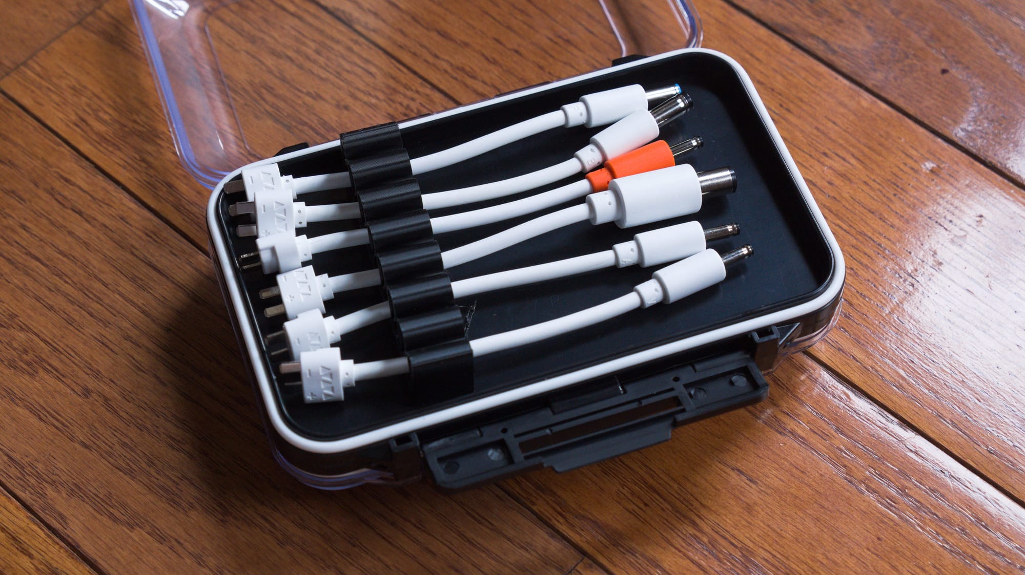 Several different end points in a case on the wood floor, connected by a 3D printed cable organizer.  