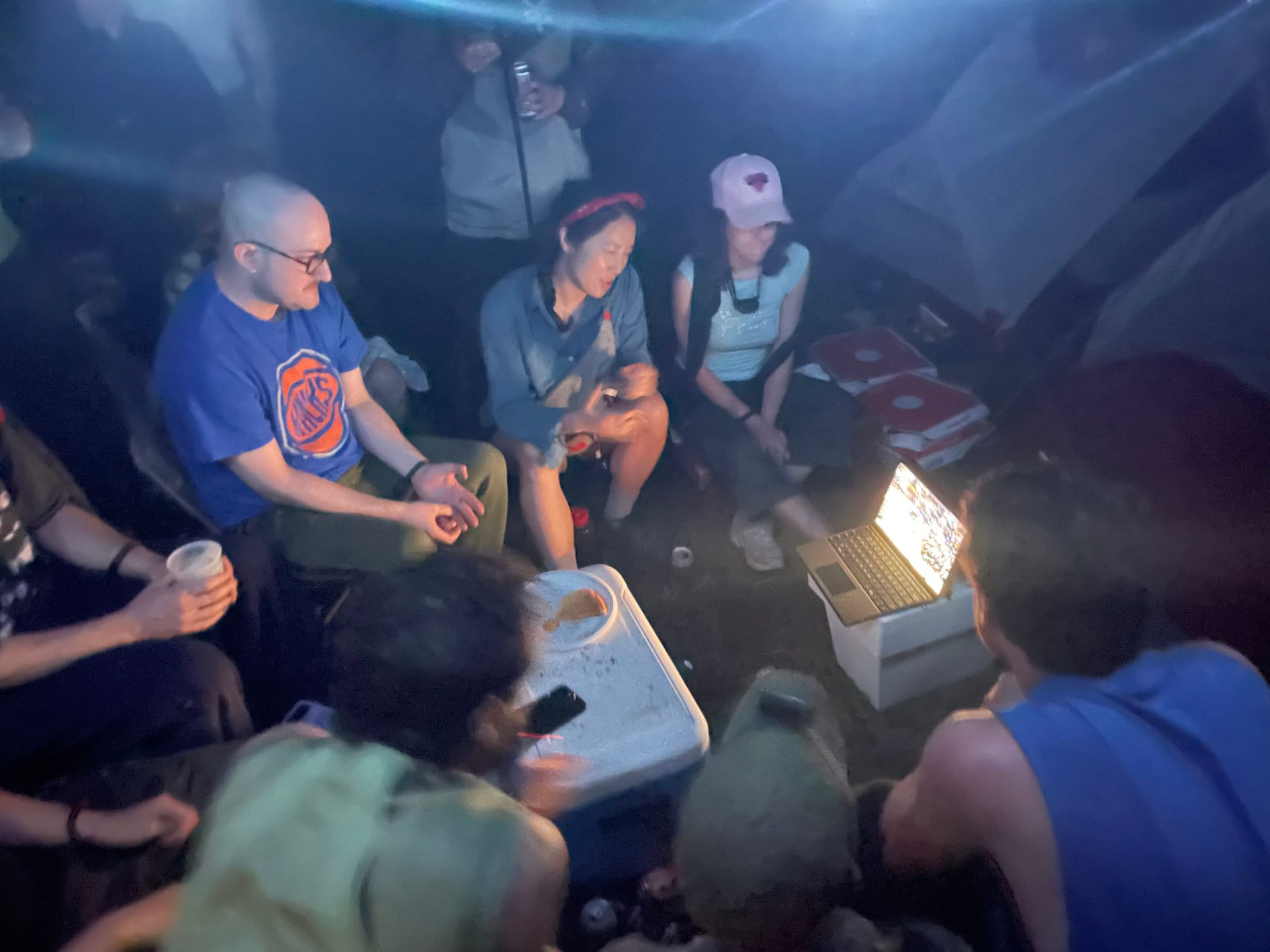 People in the woods surrounding a laptop.