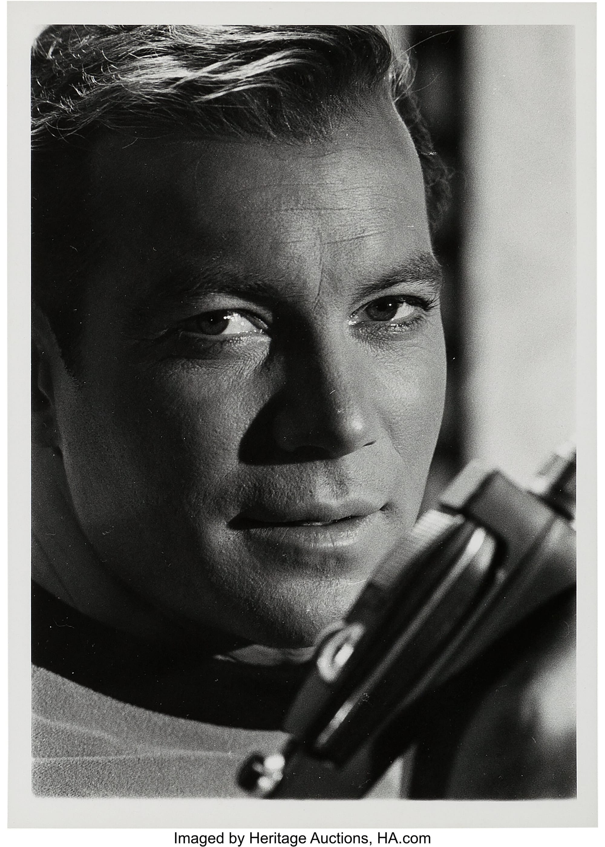 Close up shot of Captain James T. Kirk, as played by William Shatner, holding a phaser to his face. 