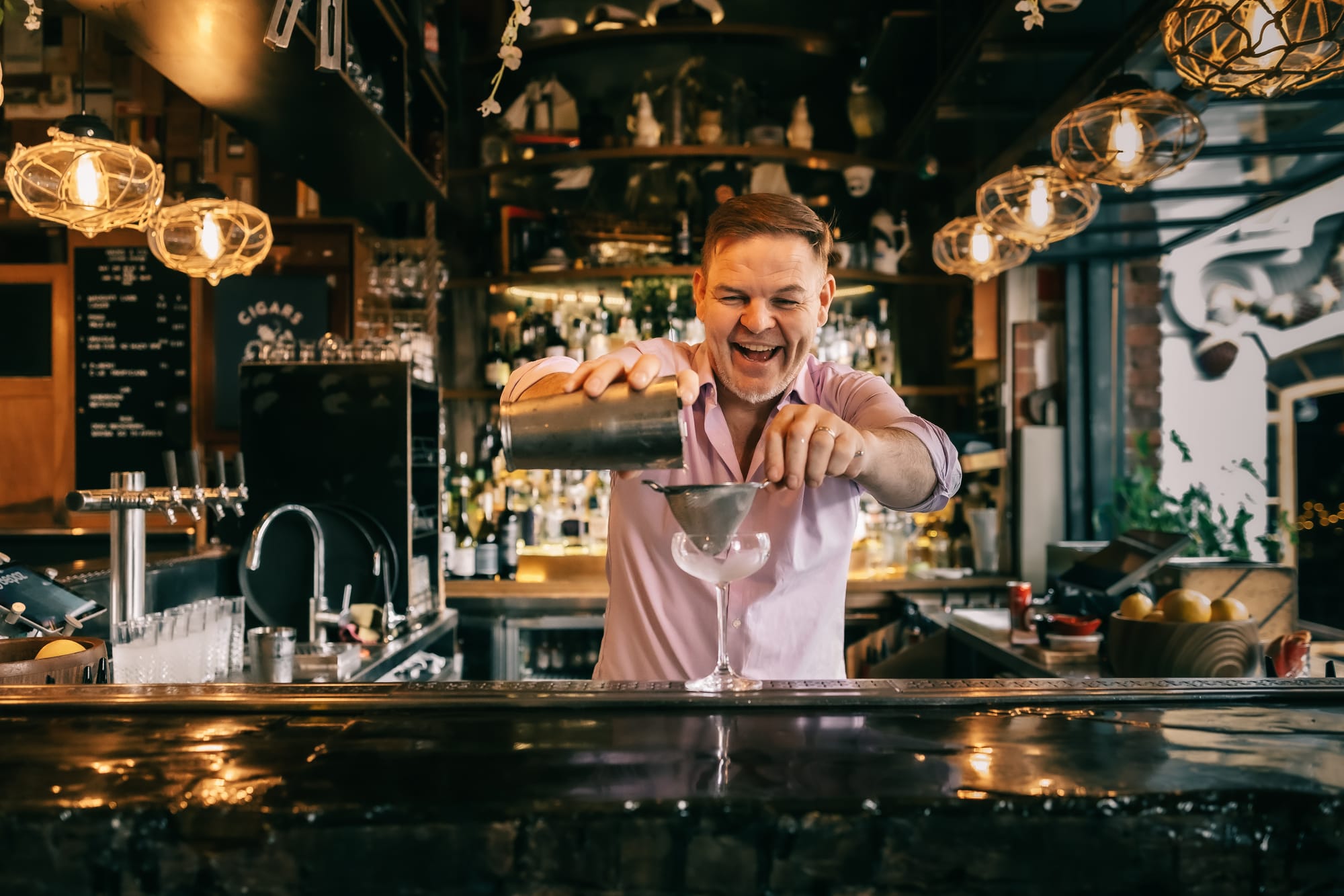 Bar tender pouring a cocktail over the bar counter