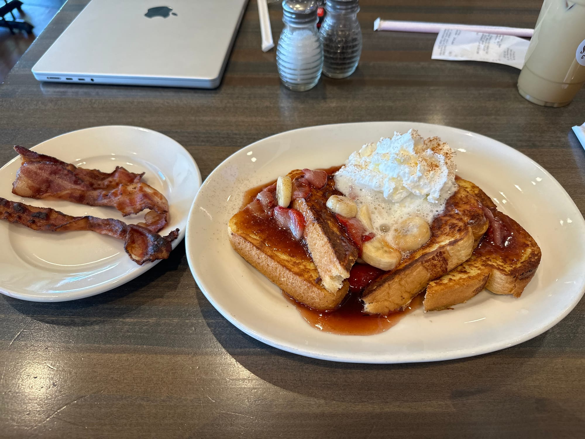 A picture of my breakfast consisting of french toast covered with fruit and a side of bacon