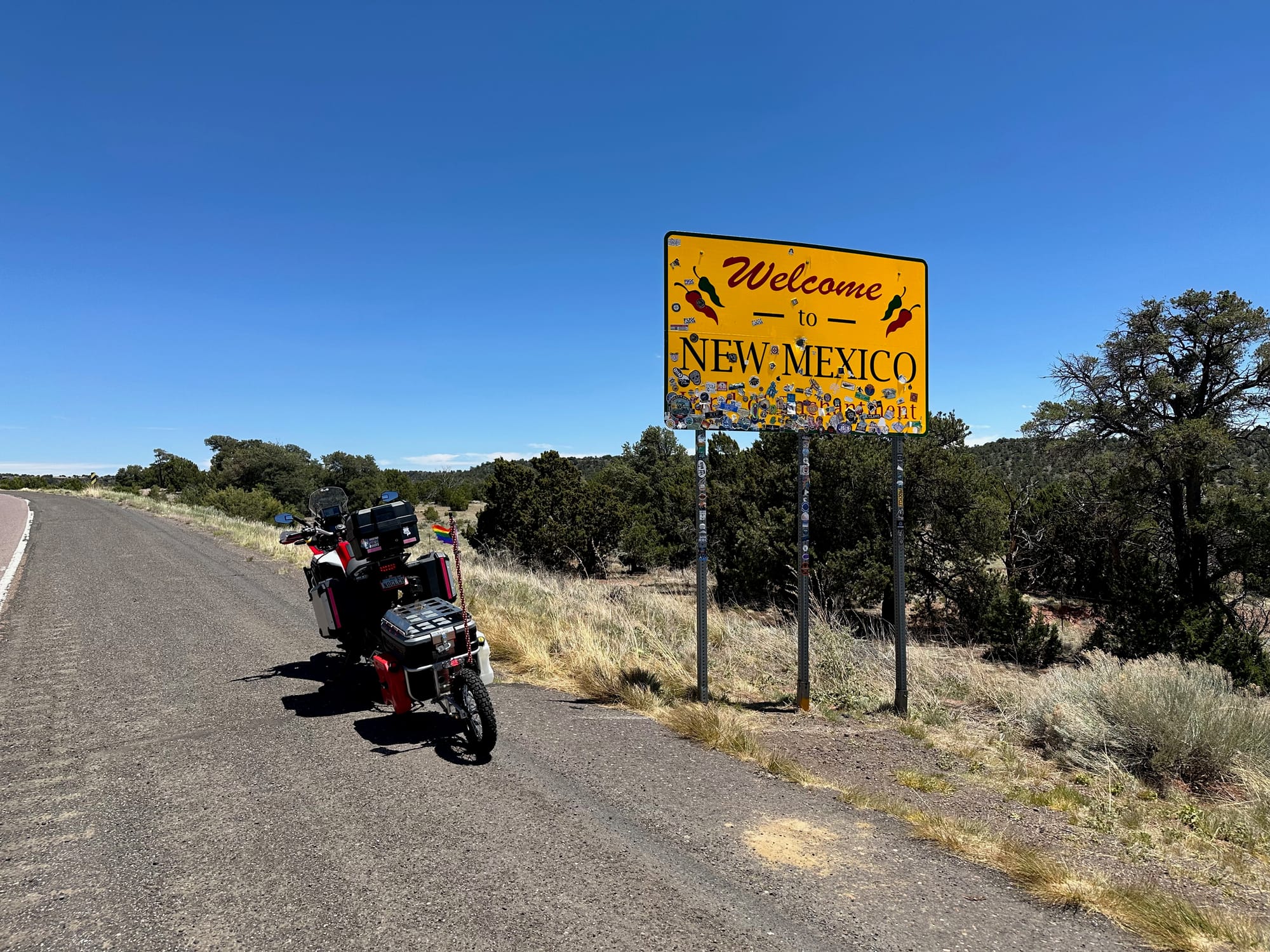 My motorcycle parked next to a yellow 'Welcome to New Mexico' sign on the side of the road