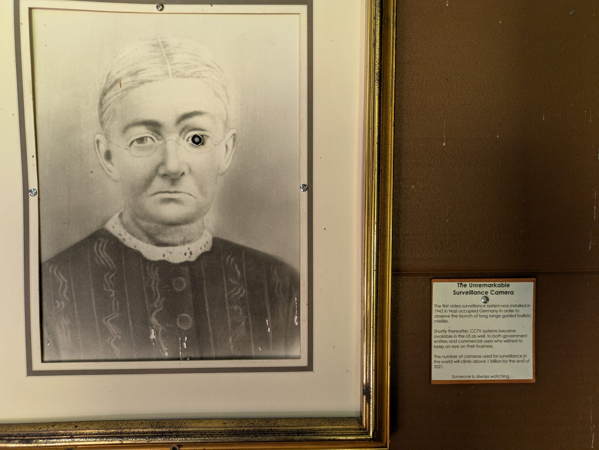 The Unremarkable Surveillance Camera, mounted in the eye of a photo of an old pioneer woman