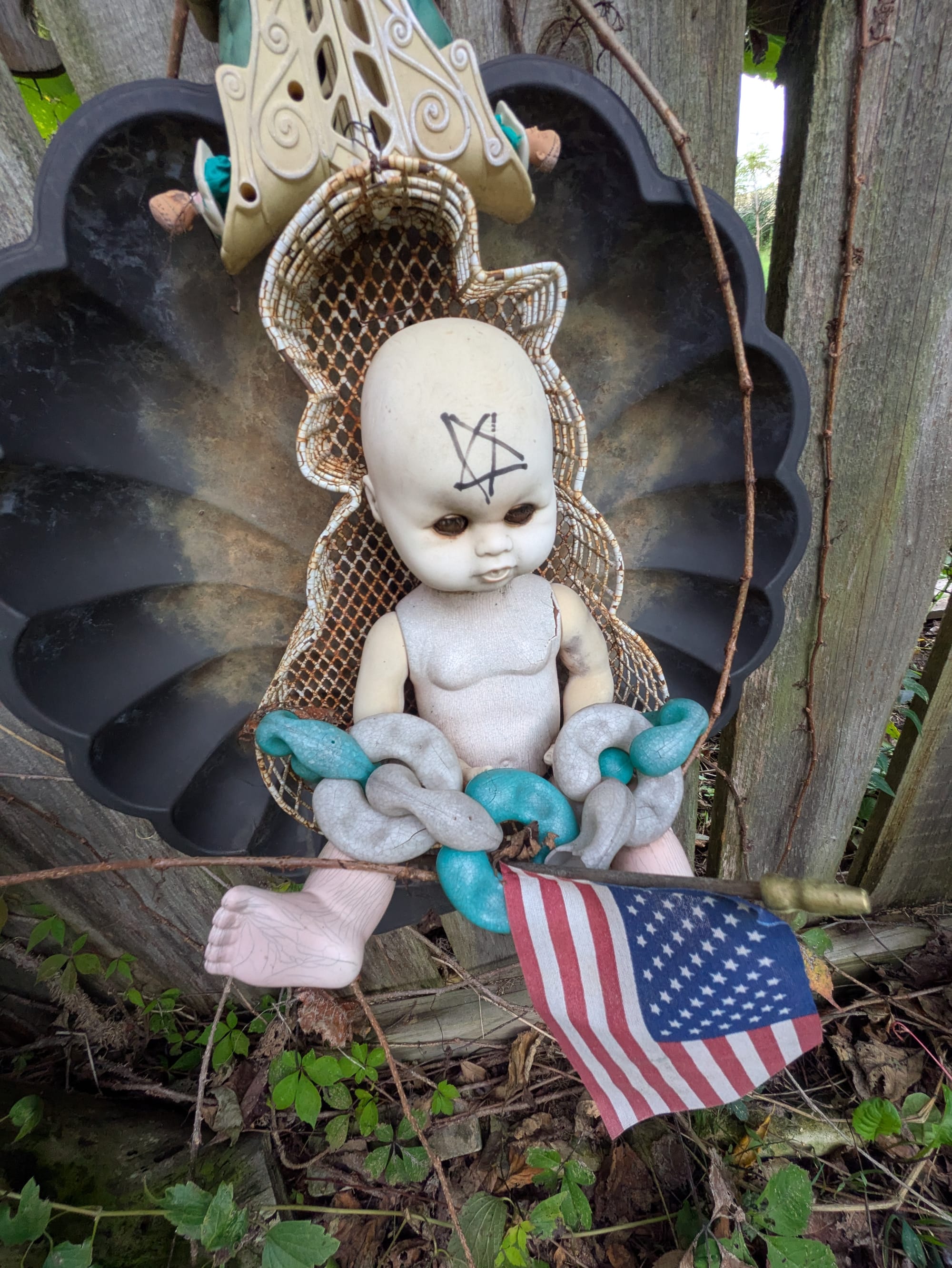A white naked doll with a pentagram drawn on its head, holding an American flag