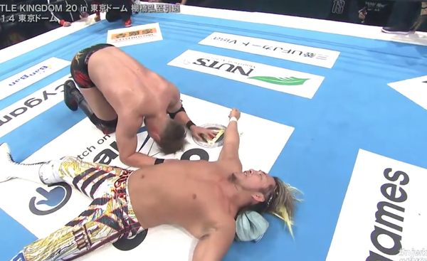Kazuchika Okada bows deeply to the beaten Hiroshi Tanahashi, who lies beaten on the mat, grinning.