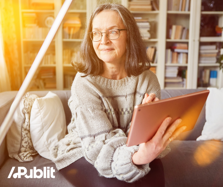 Older woman with glasses sitting on a sofa reading an ebook