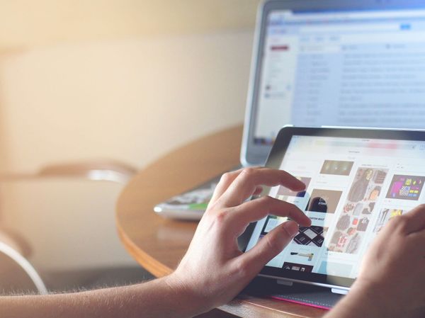 A pair of arms holding onto an ipad in from of a computer screen 