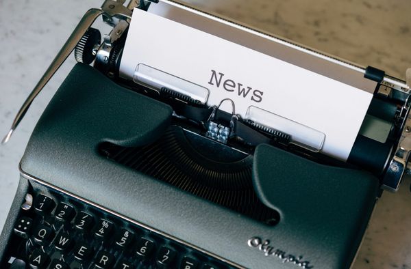 A black typewriter with a piece of paper saying news