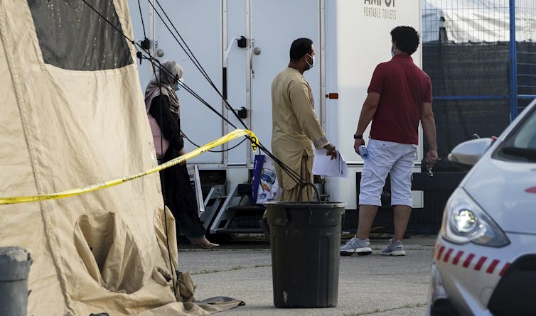 Two men and a woman in a hijab preparing to board a bus.