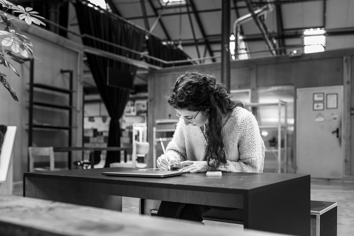 Black and white photo of a brown hair woman drawing on an iPad in a shared co-working space in Montpellier