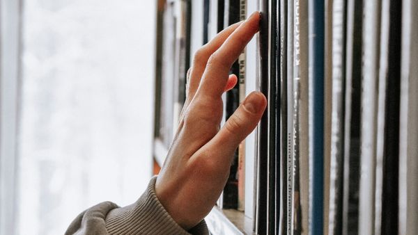 Woman's hand touching lightly the cover of a book on a book shelf.