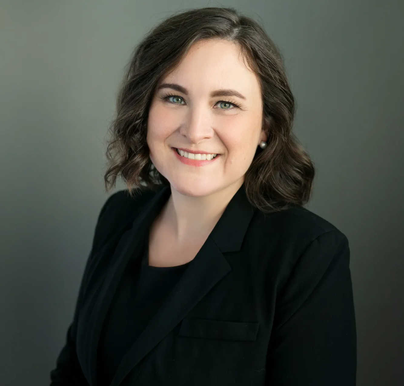 A woman with short brown hair wearing a black blazer smiles at the camera.