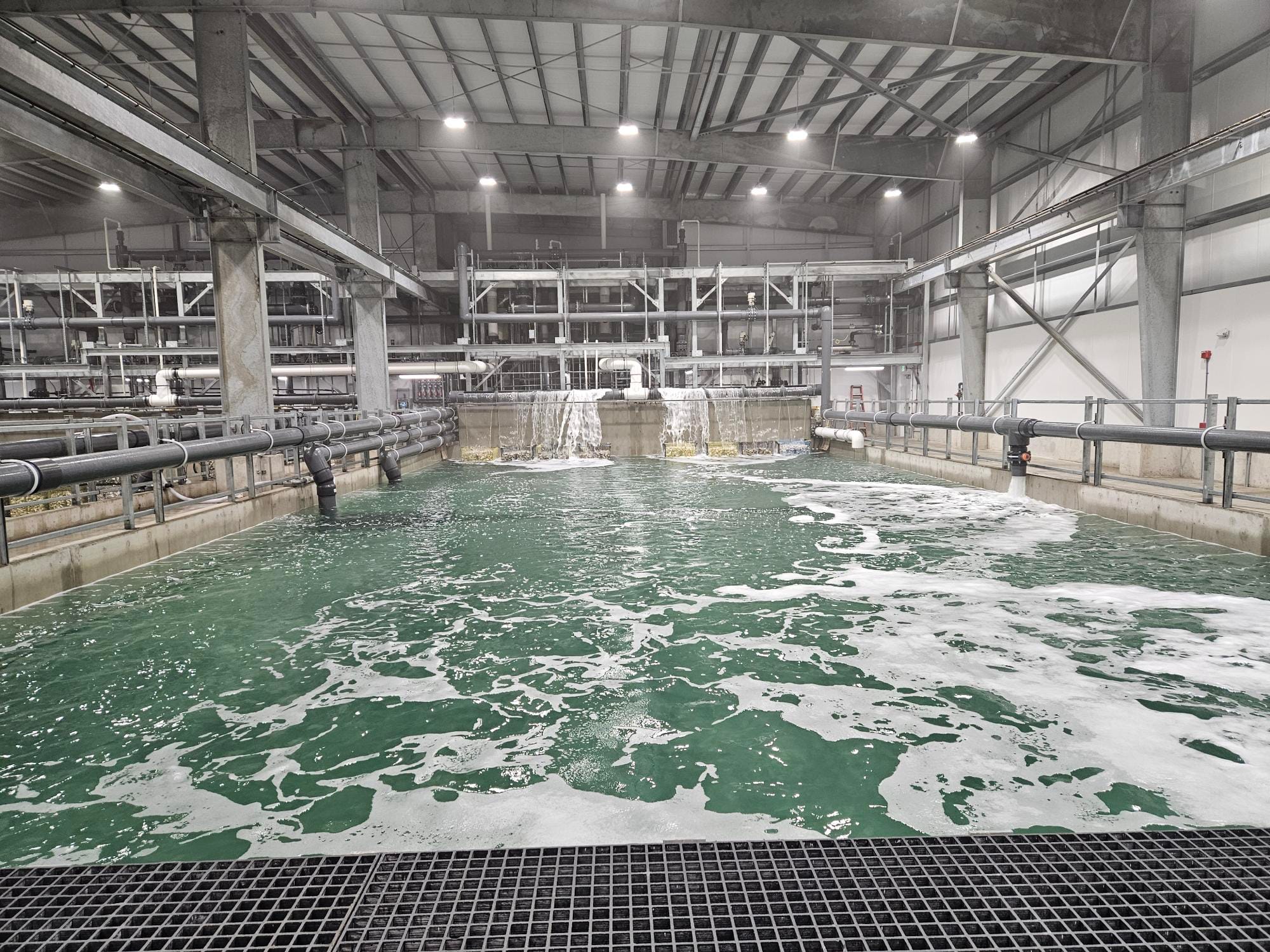 A brightly lit industrial facility with a large tank of water surrounded by pipes.