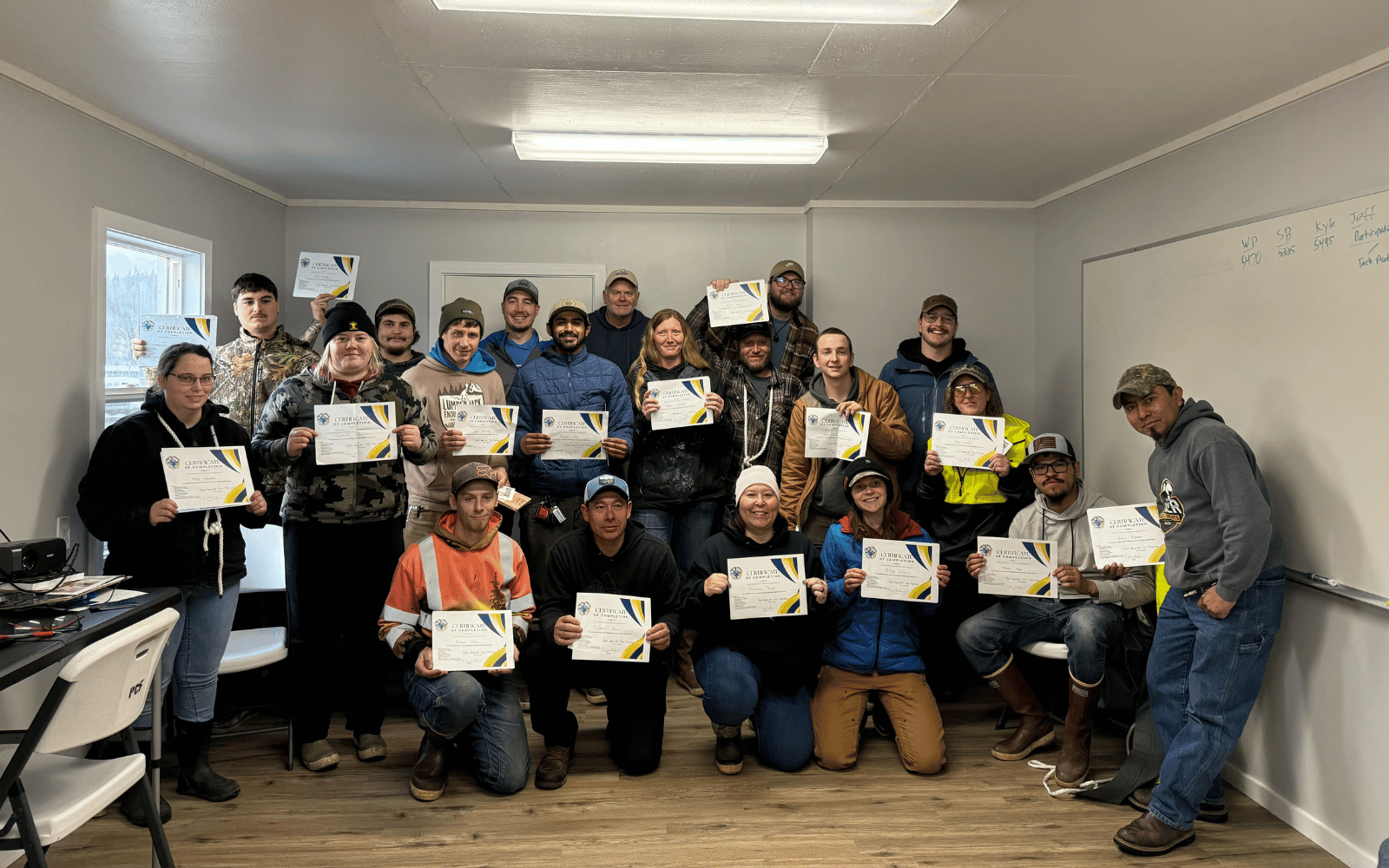A group of 20 people pose with pieces of paper in a classroom.