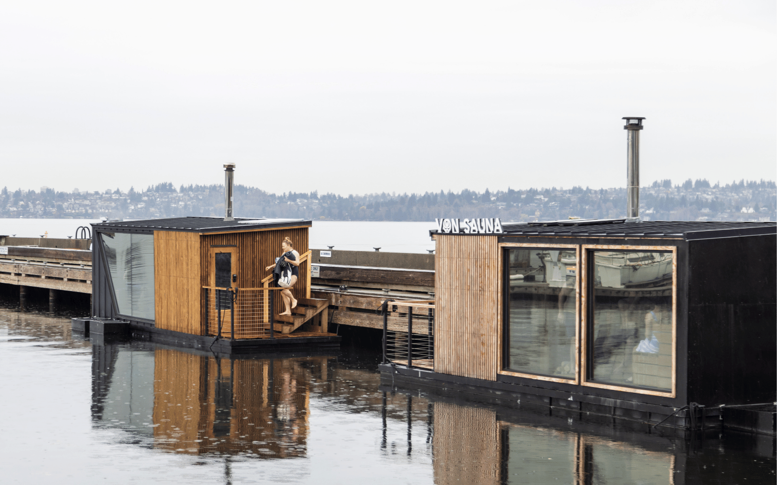 Two black and wood rectangular structures with chimneys float next to a pier.