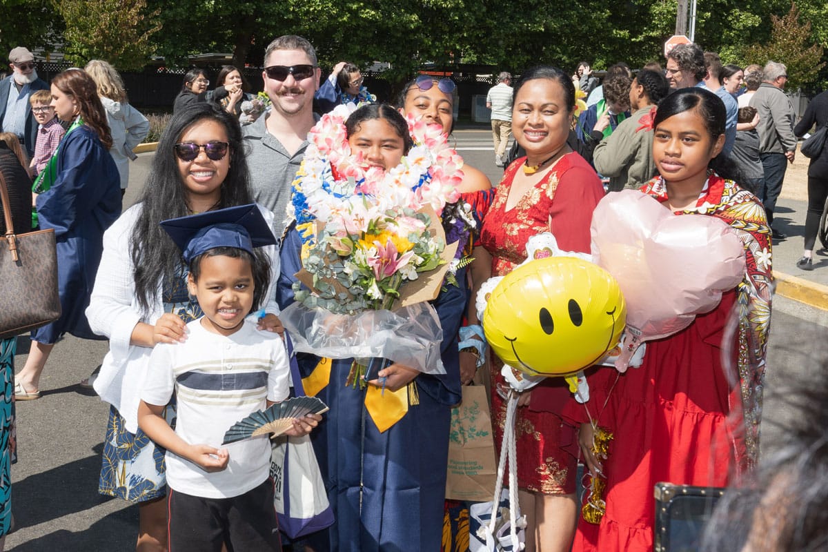 A family surrounds a graduate holding flowers and covered in lei.