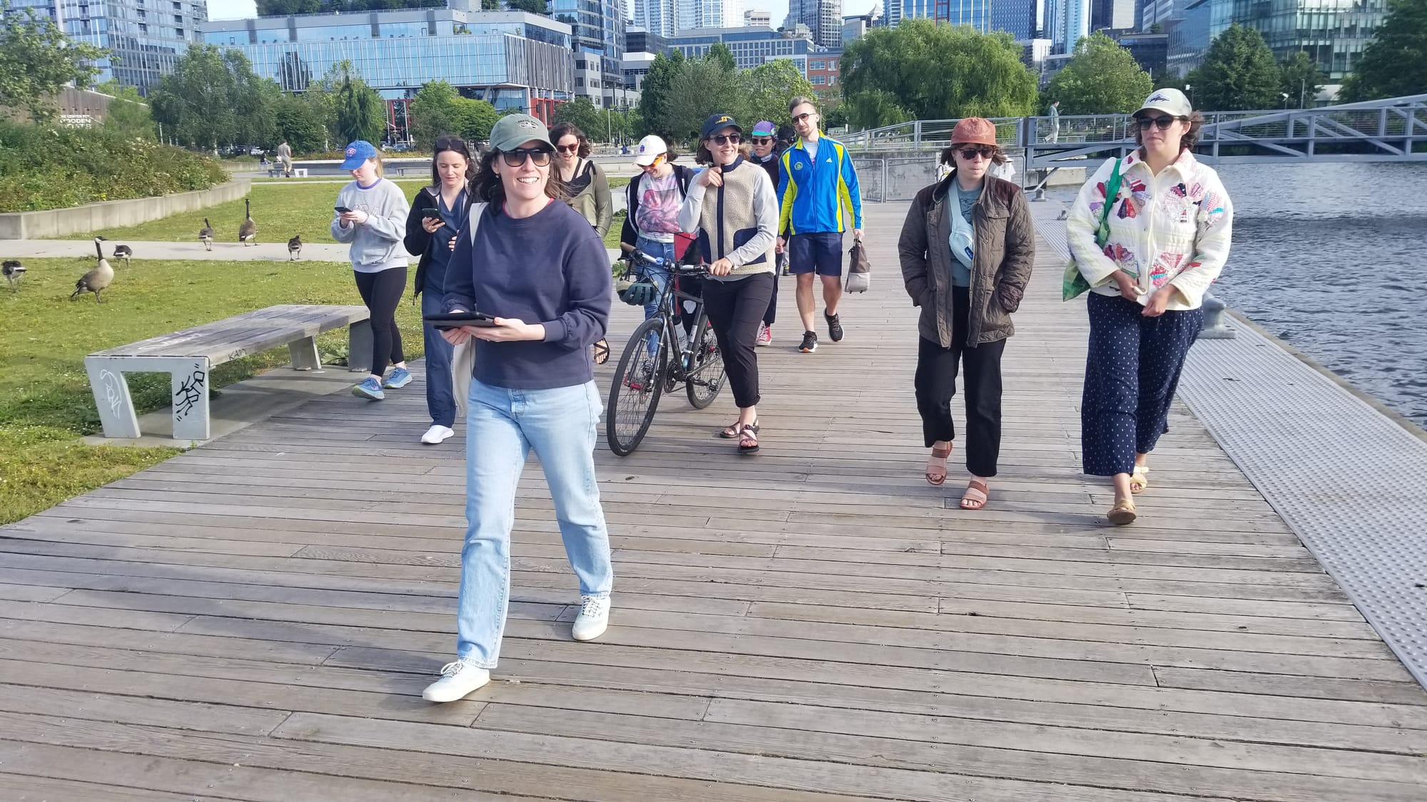 A woman in a baseball cap and sunglasses smiles leading other people through a park.