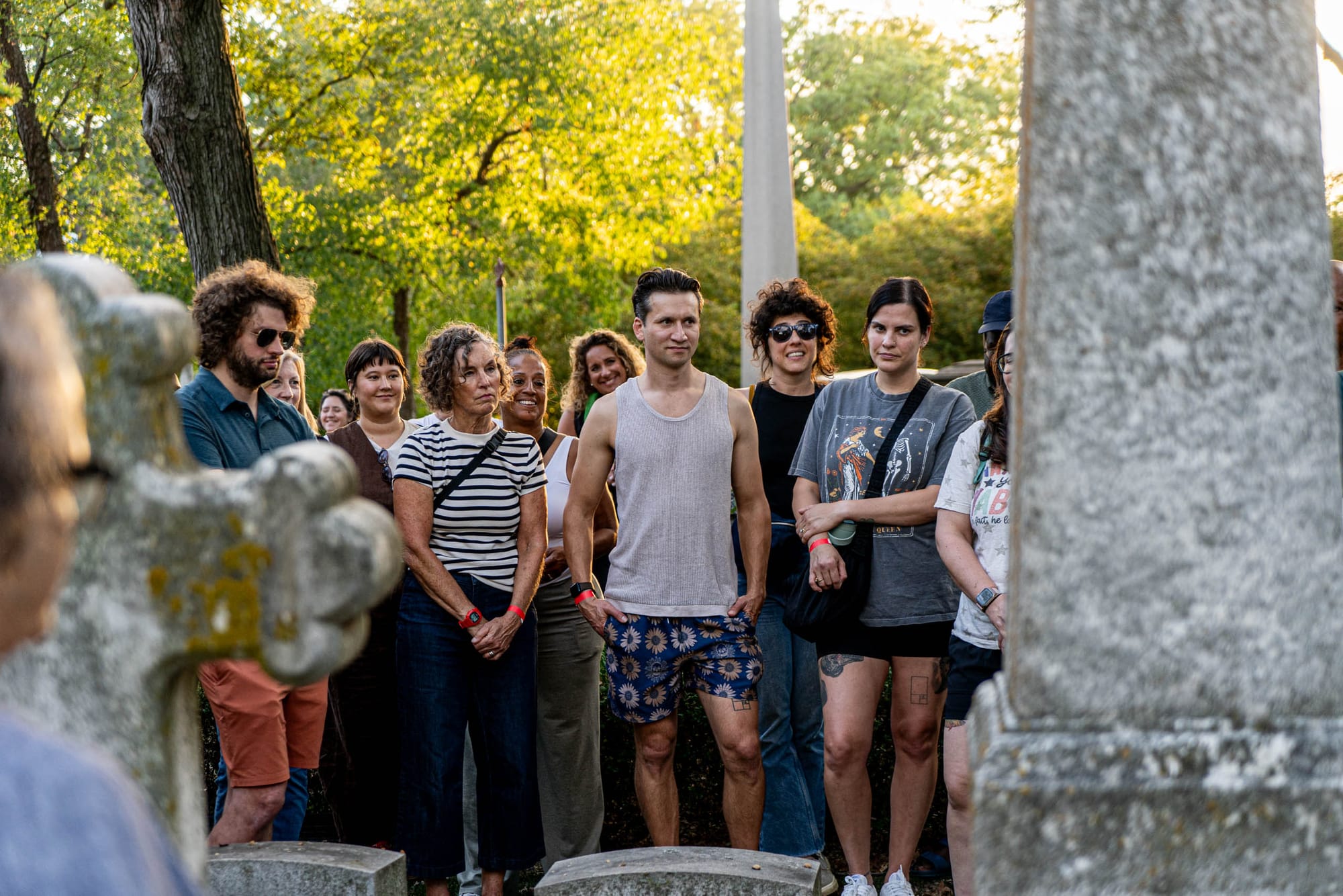 A dozen people are visible between tombstones on a sunny day.
