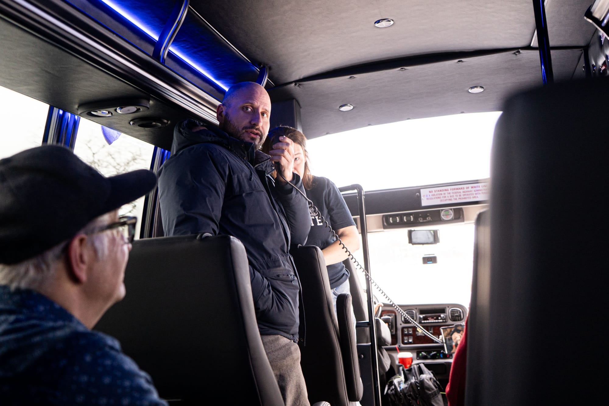 A man speaks into a microphone inside a bus.