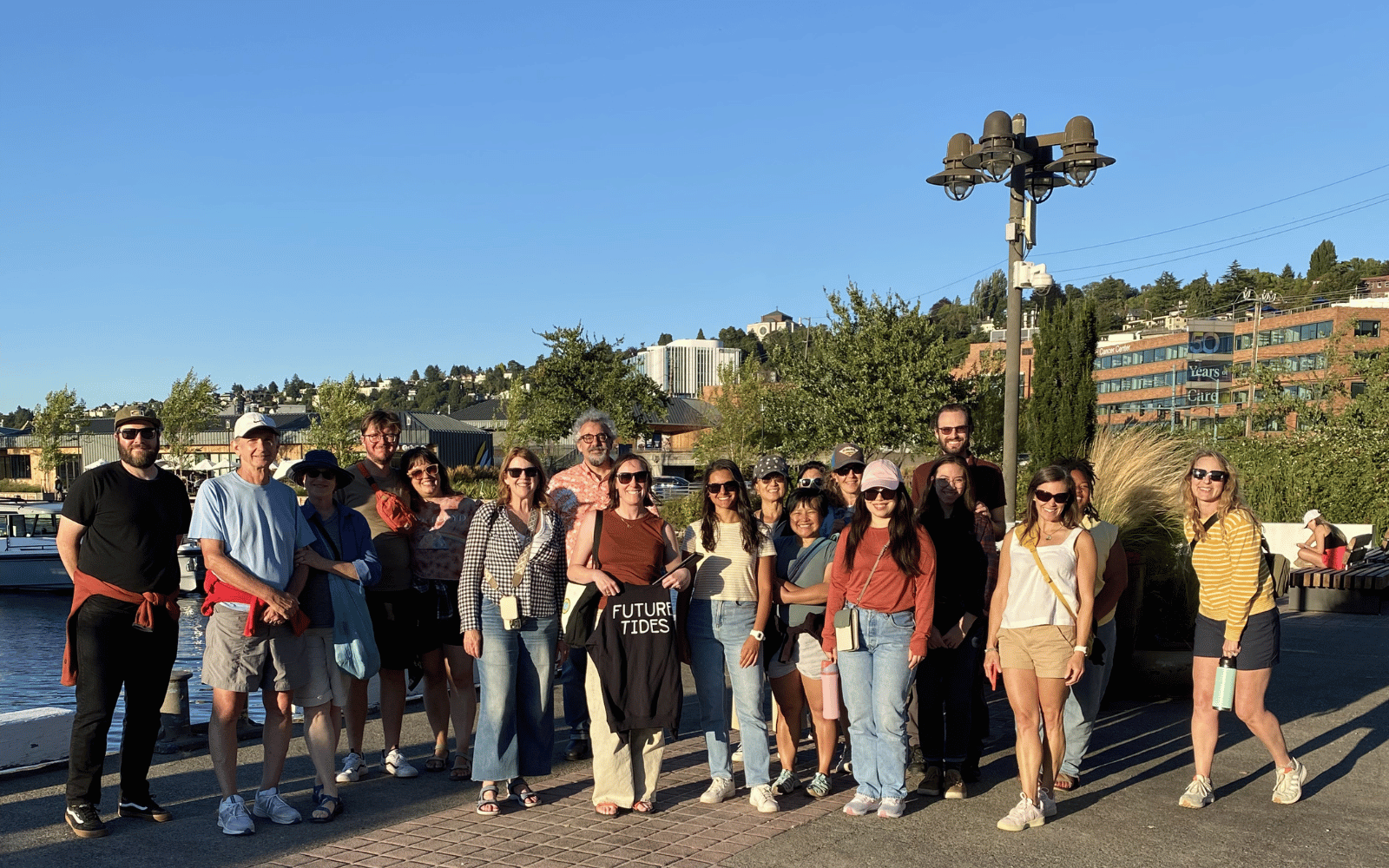 A group of about 20 people pose near a body of water on a sunny day.