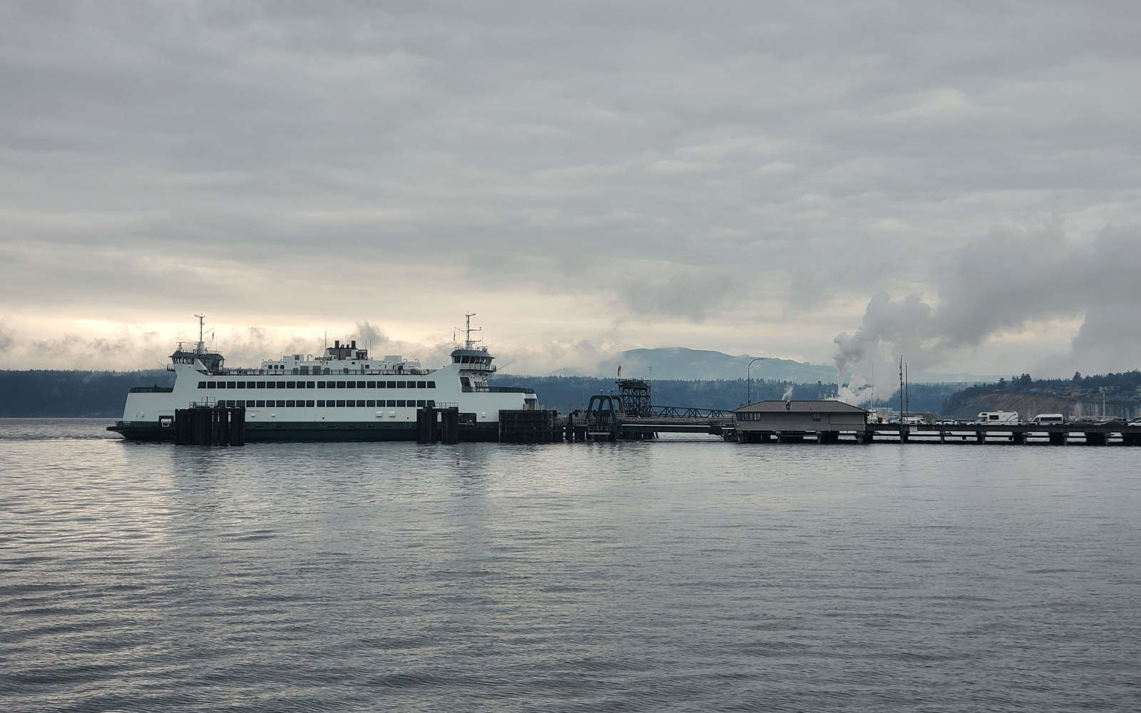 A large white boat at a dock with cars lined up to board.