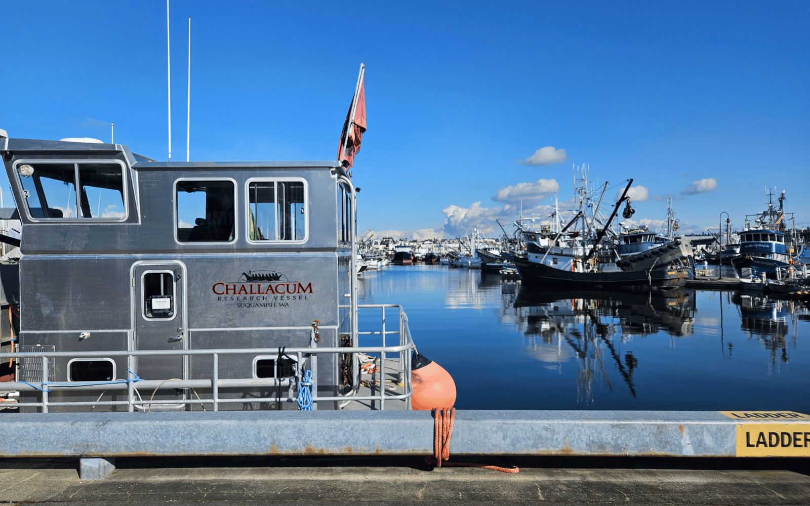 An aluminum boat that reads on the side "Challacum Research Vessel" with fishing boats behind.