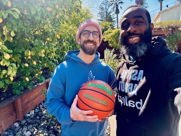 Tim and Frank outdoors on a sunny day, Tim holding a basketball in a blue hoodie and pink beanie, Frank in a black 'Ask me about Ballers' hoodie. Lemon tree in background.