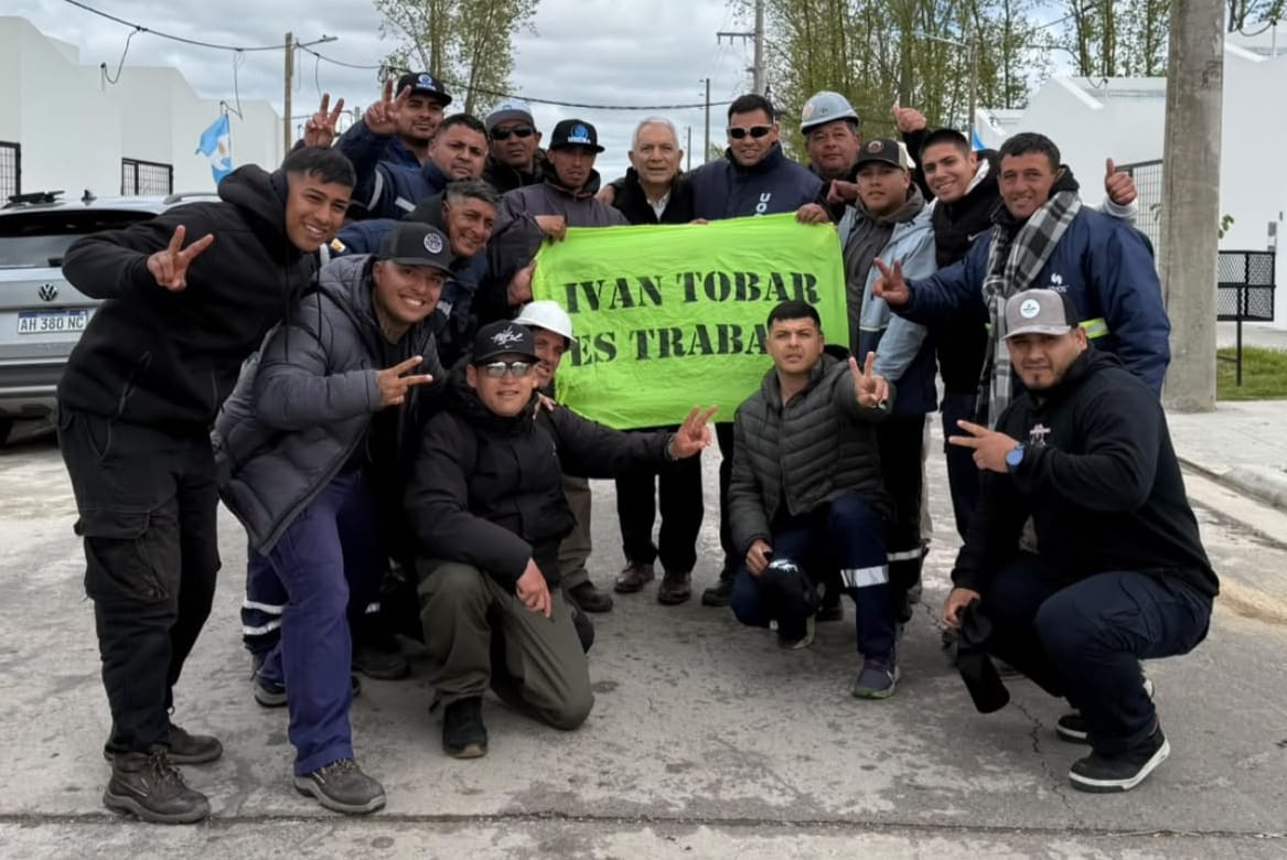 Integrantes de la Juventud de Trabajadores Unidos de UOCRA La Plata posan con el gobernador Axel Kicillof y banderas del gremio frente a las viviendas entregadas en Melchor Romero.