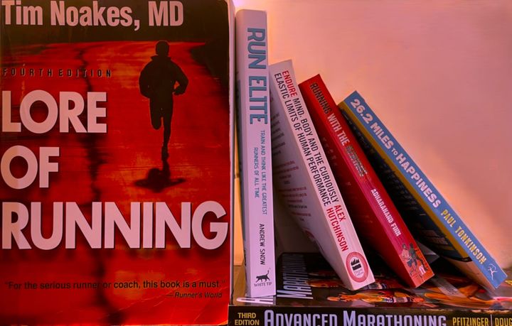 Bookshelf with classic running titles including Lore of Running, Run Elite, Endure, Running with the Kenyans, 26.2 Miles to Happiness, and Advanced Marathoning.