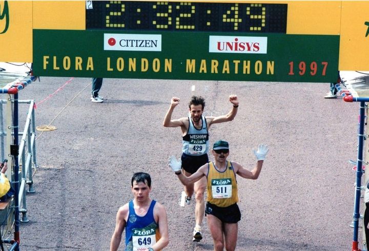 Pete Johnson finishing the 1997 Flora London Marathon in 2:32:49, raising his arms as he crosses the line behind two other runners.