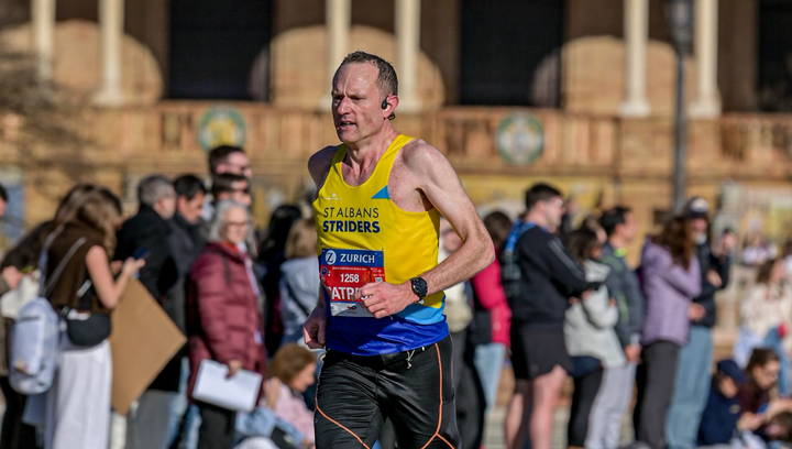Runner in St Albans Striders vest racing mid-marathon at Seville, focused and working hard, with spectators blurred behind during a fast, flat city-centre section.