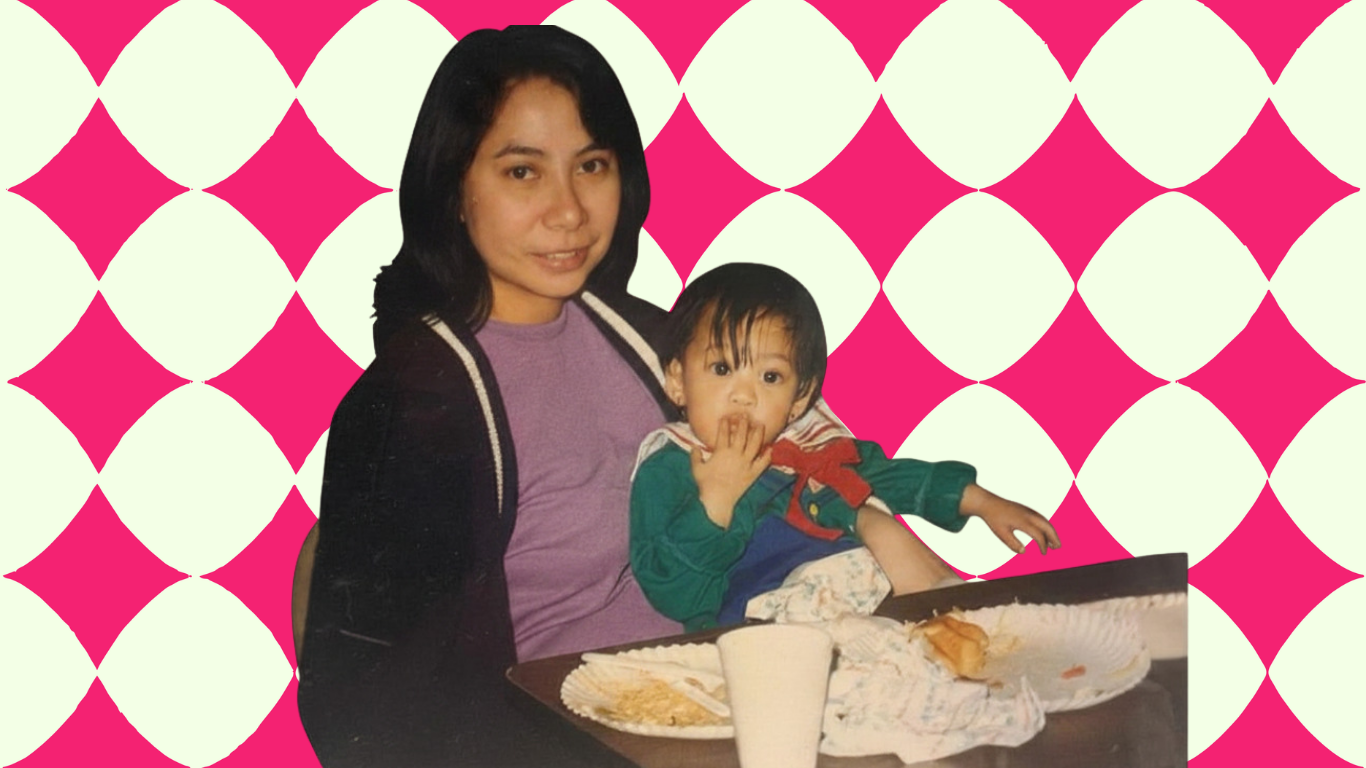 A woman holds a baby, who has her hands in front of her mouth. On the table in front of them are the remains of food on paper plates.