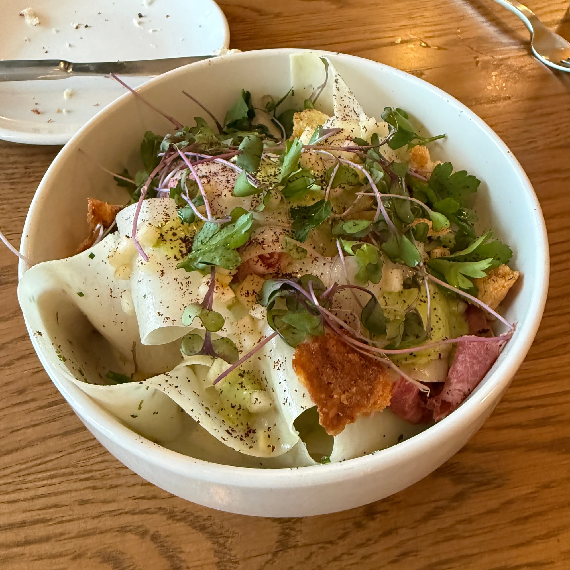 A bowl with kohlrabi ribbons, microgreens, and crispy beef tongue pastrami