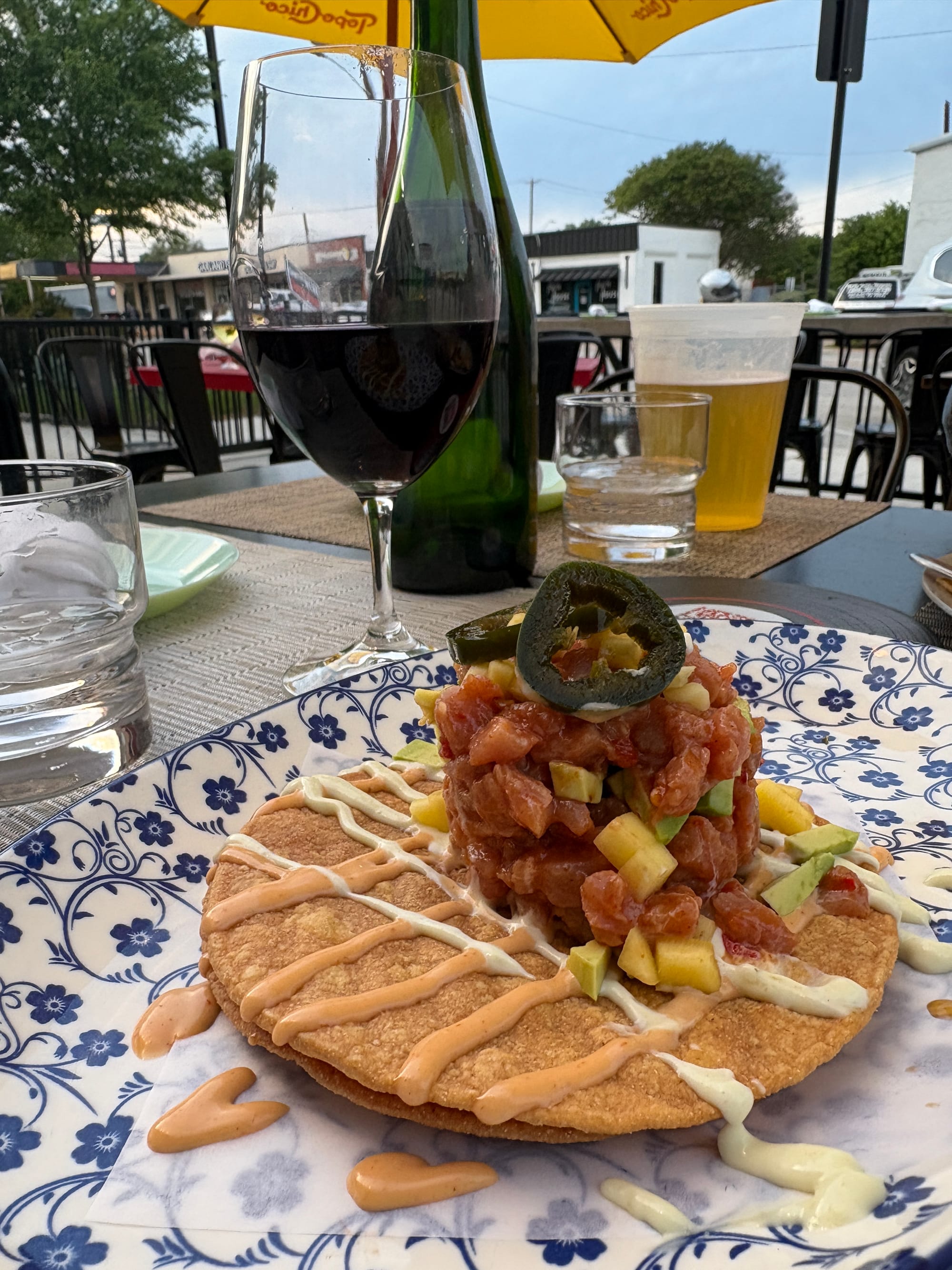 A tostada with a stack of tuna topped with aioli and pickled jalapeños, with a glass of red wine.