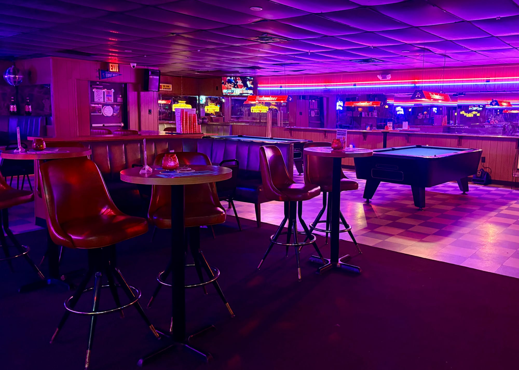 A bar with neon lights, pool tables, and leather booths at night.
