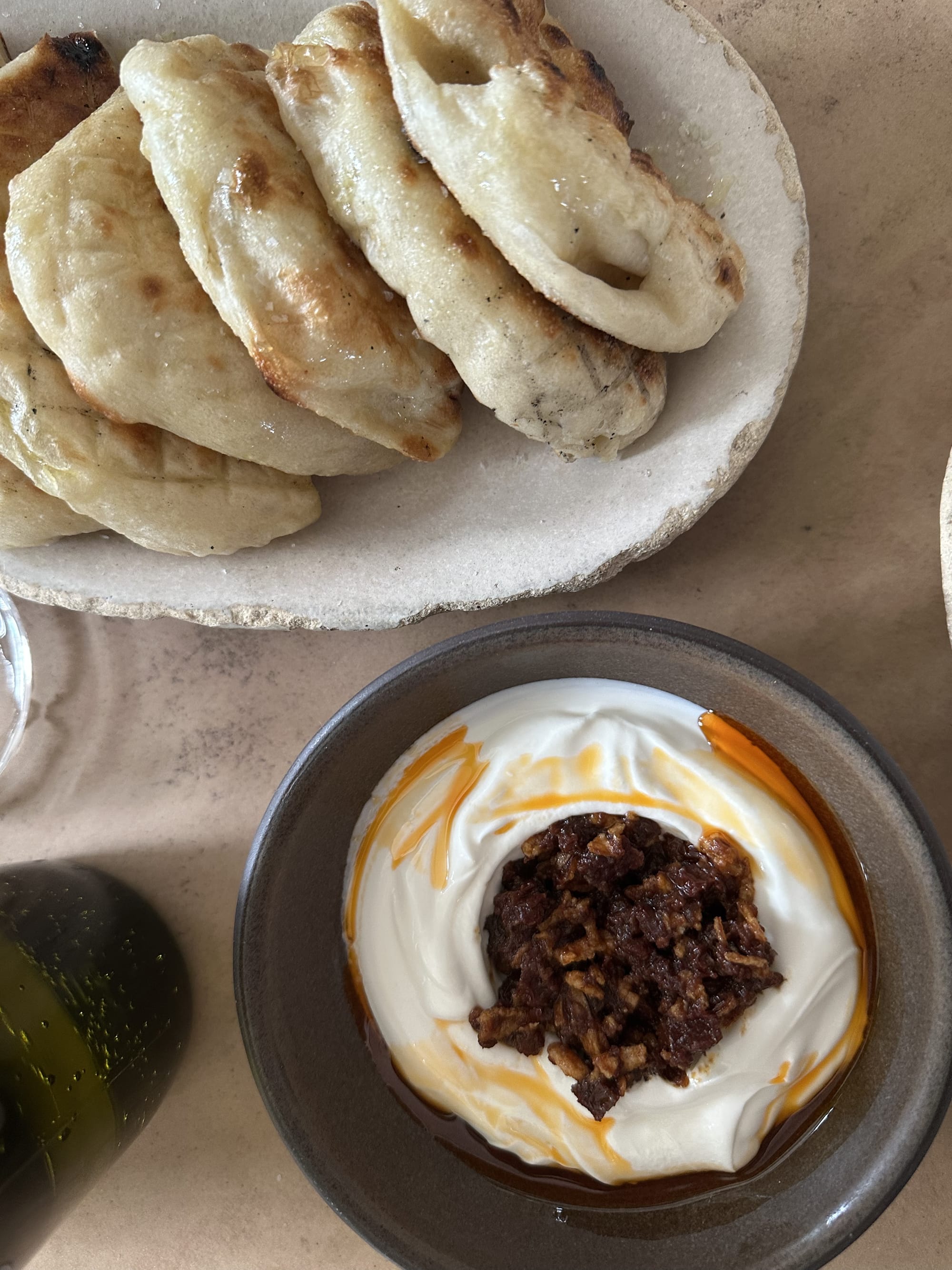 Labneh in a bowl topped with salt cod XO sauce. A plate of laffa bread can be seen in the background.