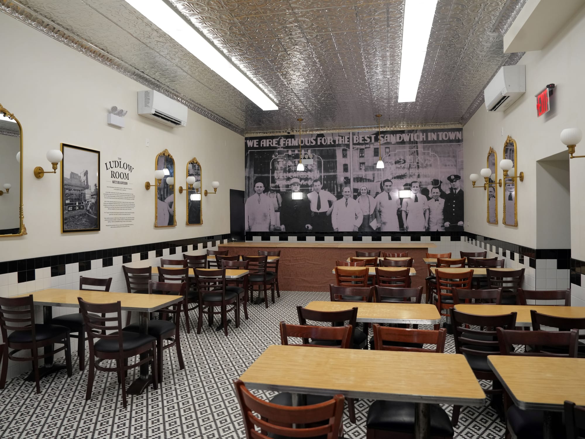 A dining room with wooden tables, mirrors on white walls, and black and white tiled flooring.