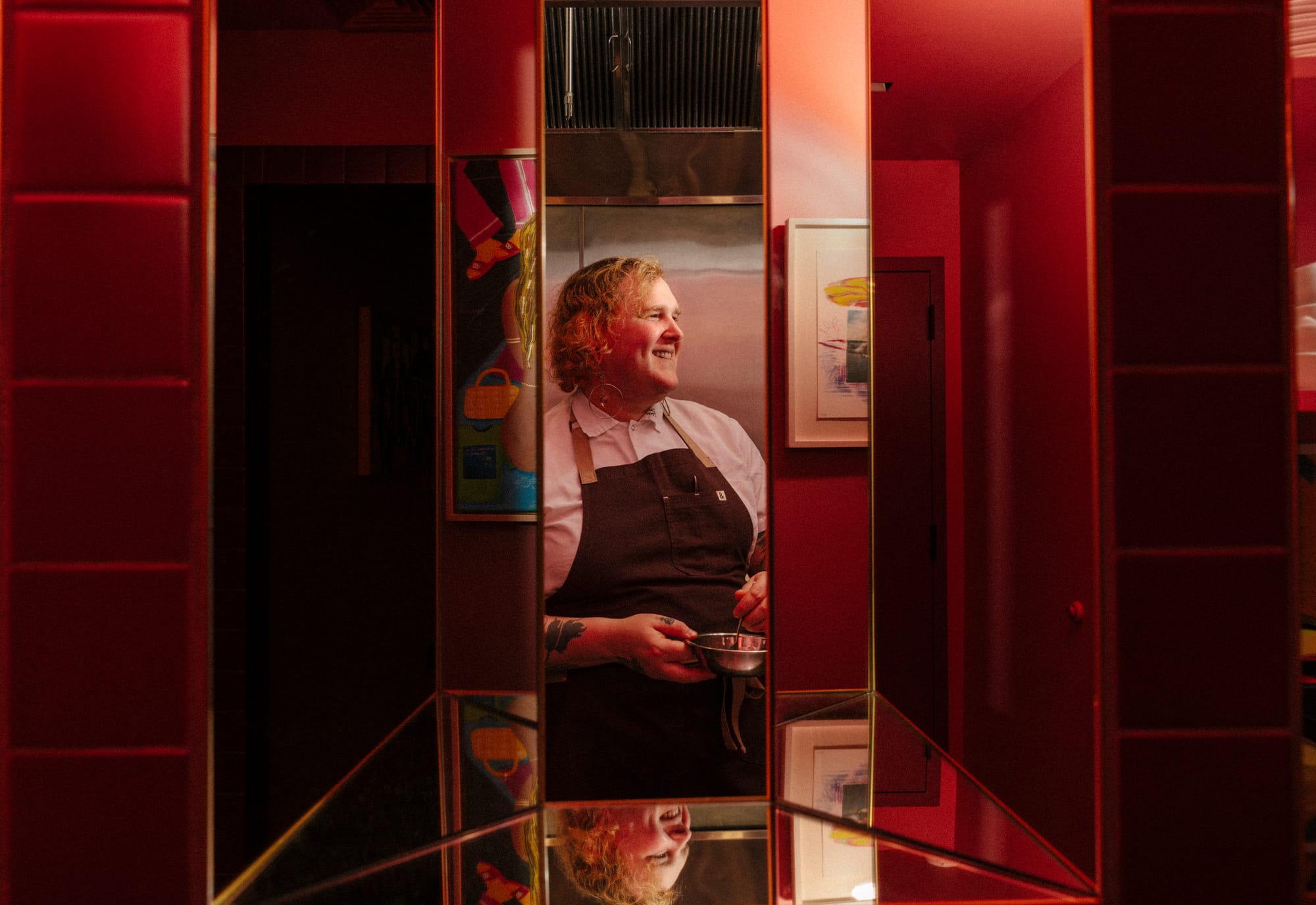 Chef Telly Justice, with short blond hair and an apron, framed between two mirrors