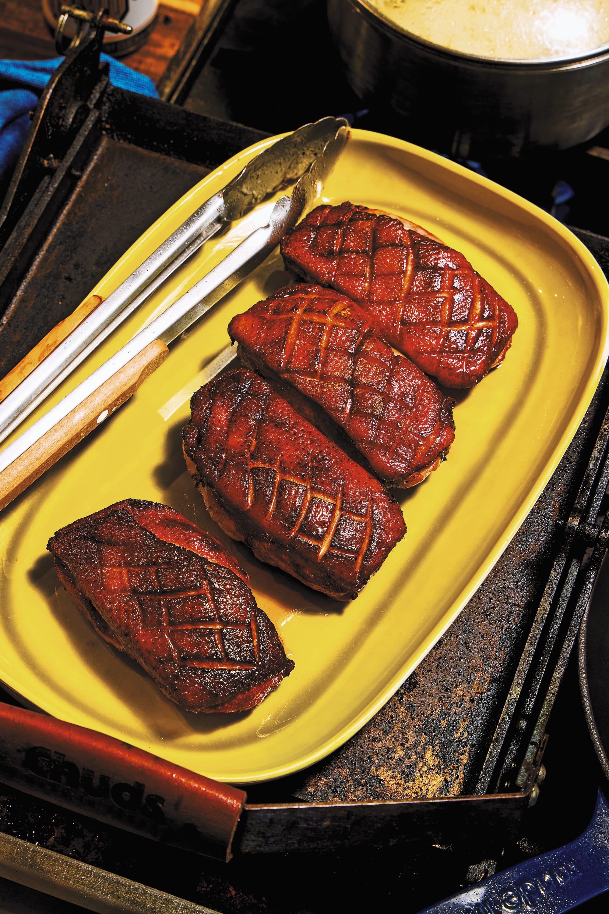 Three smoked duck breasts sit on a yellow plate, on top of a grill.