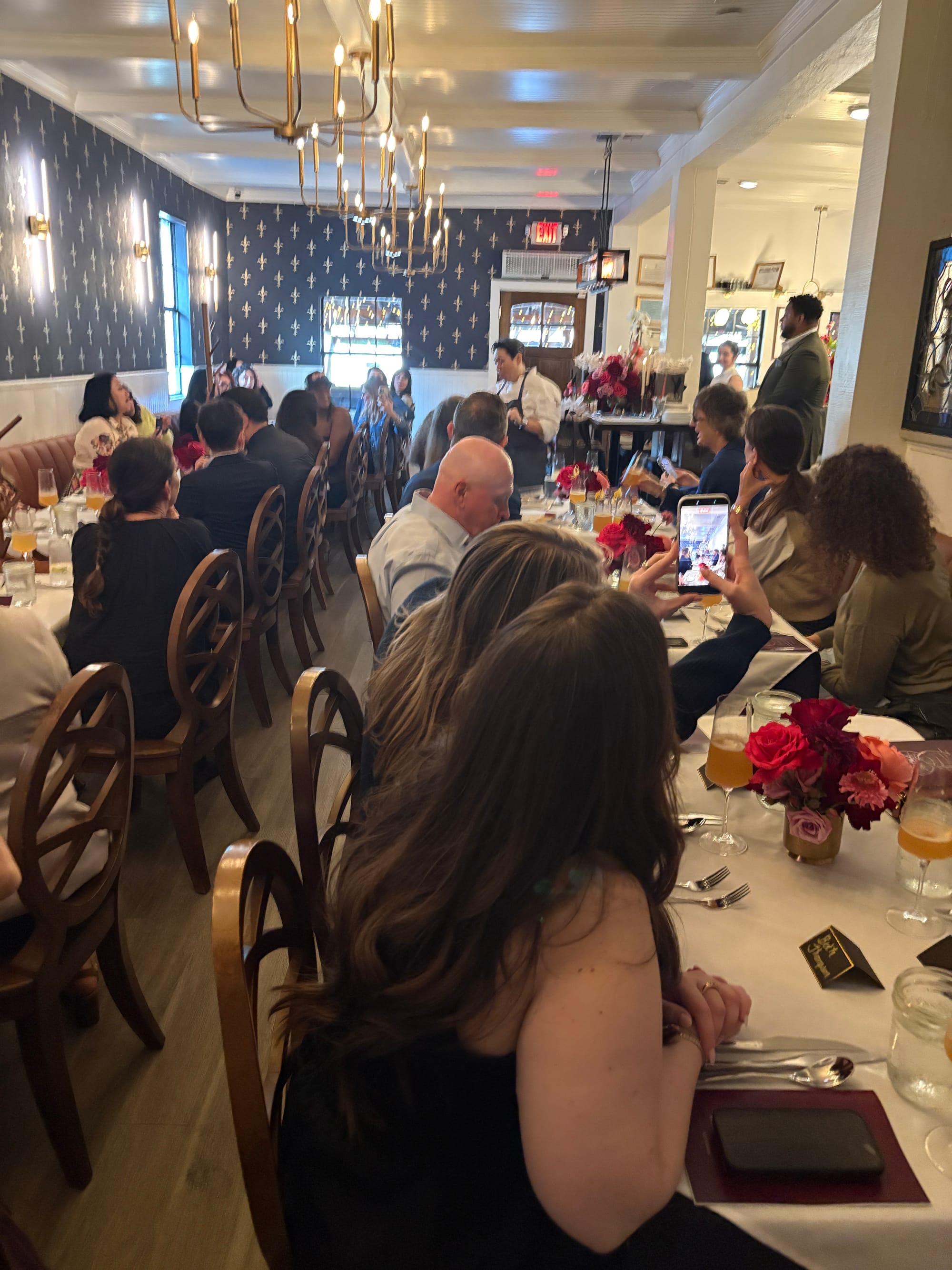 A woman in a chef's coat speaks to a room full of diners.