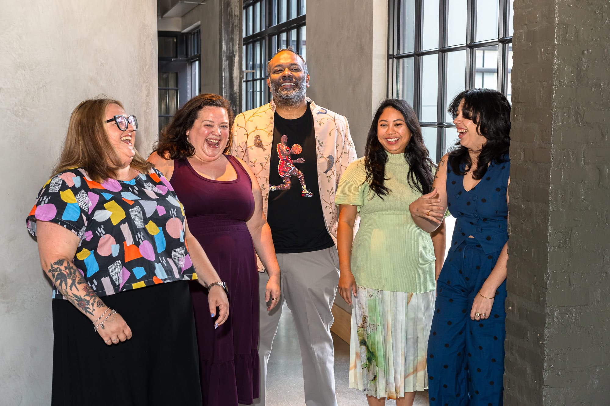 The five members of Ravenous posing together in a hallway with windows and smiling.