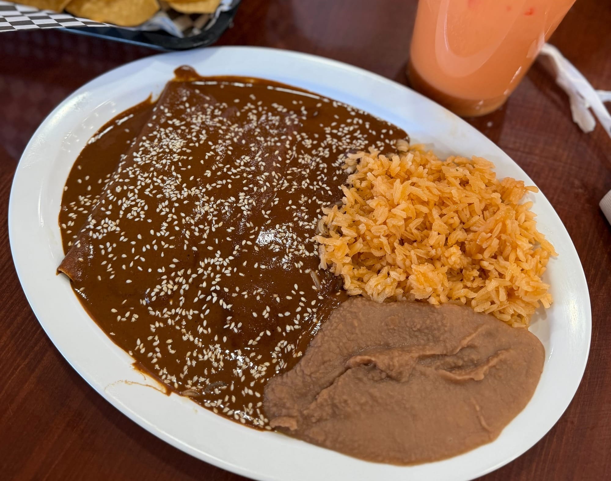 A plate of enchiladas covered in brown sauce and sesame seeds served with rice and beans.