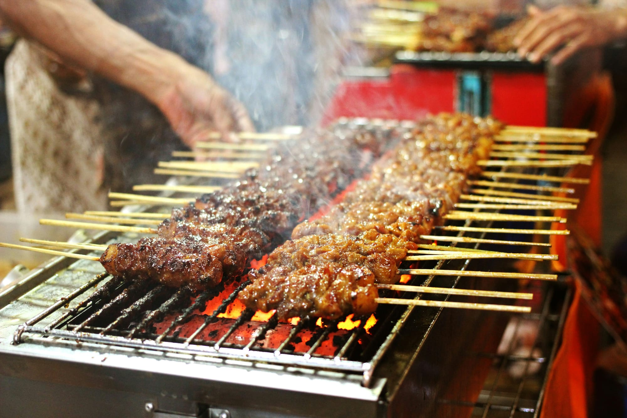 A grill with metal grates cooks several meat skewers.