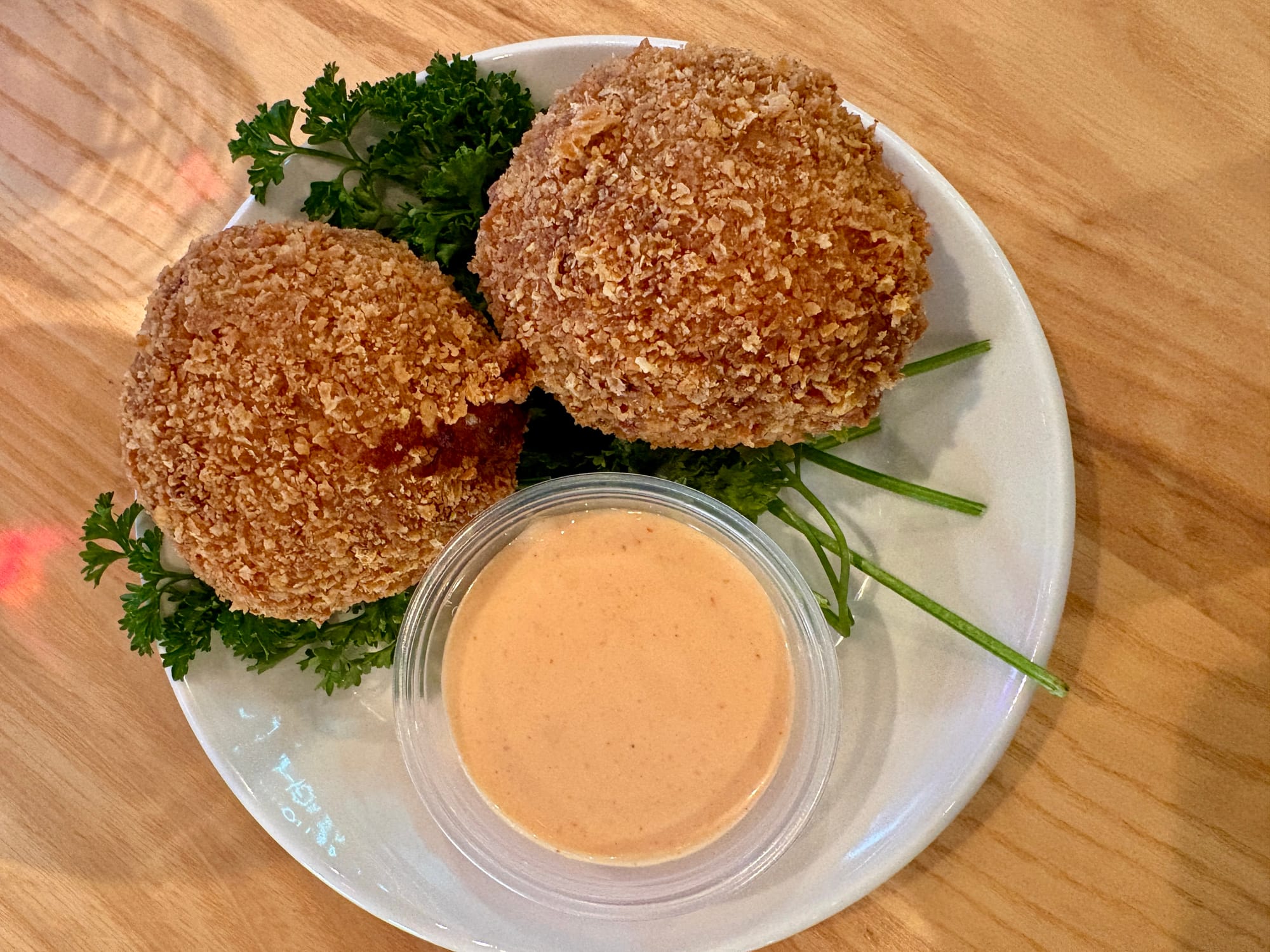 A plate holds two deep-fried balls coated in Panko crumbs and an orange dipping sauce.