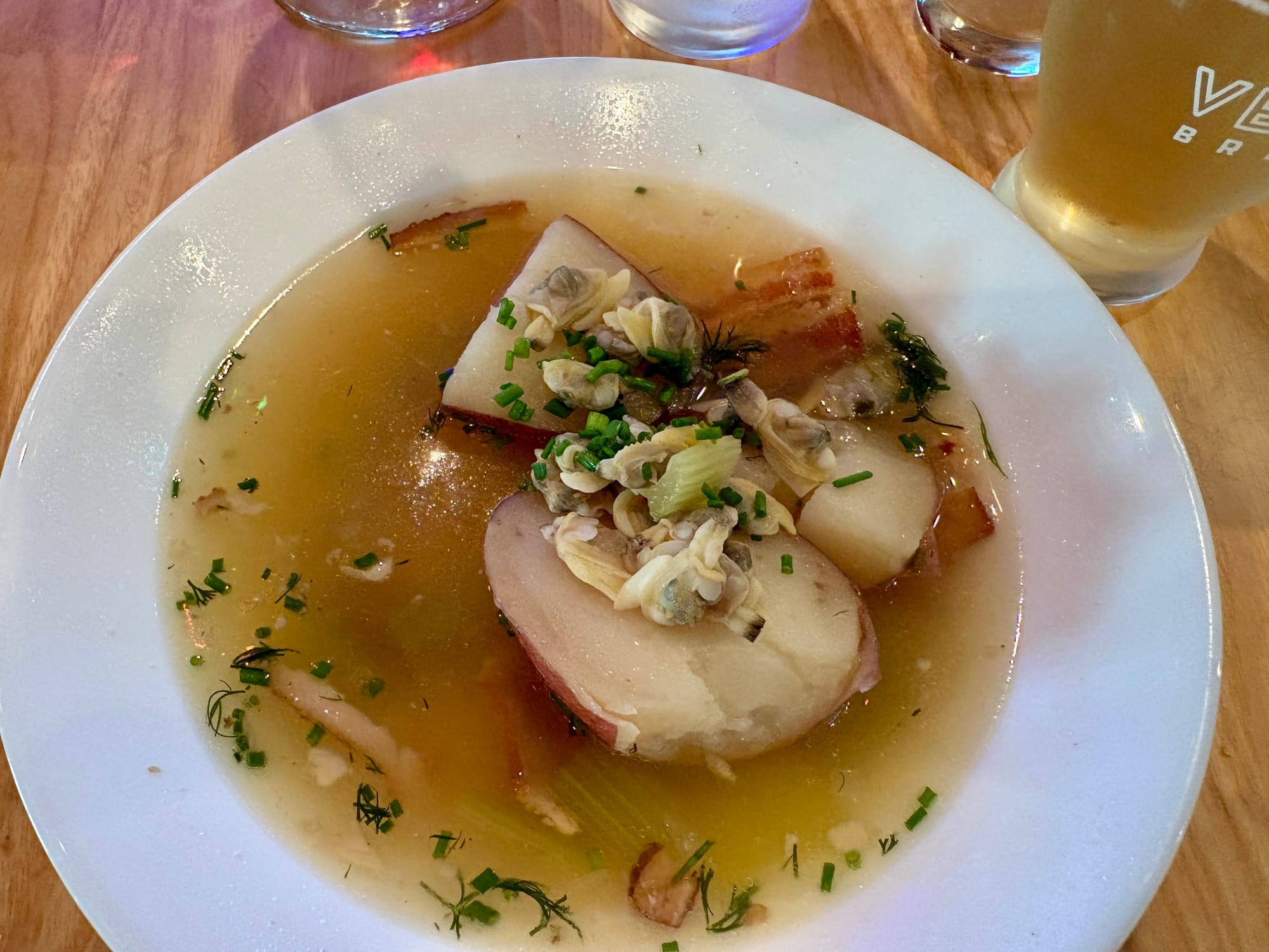 A bowl holds chicken broth, potatoes, herbs, and bacon.