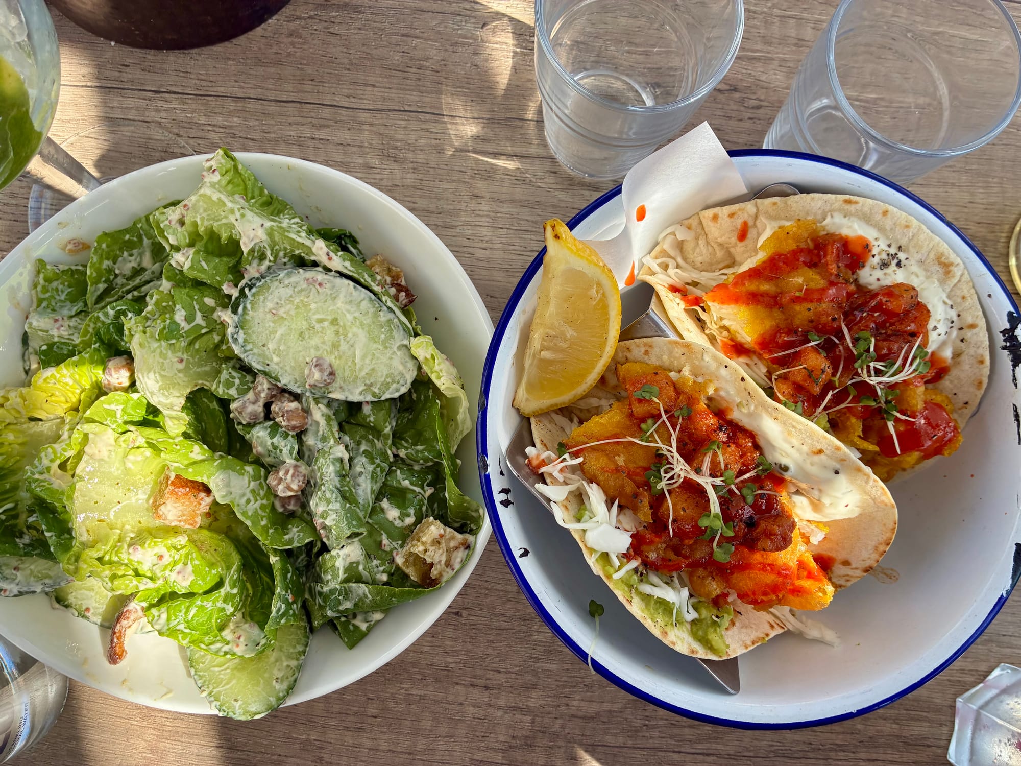 On the left is a Cesar salad with chickpeas, cucumber slices, Romaine lettuce, and crutons. On the right are two fish tacos topped with violently red pineapple salsa.