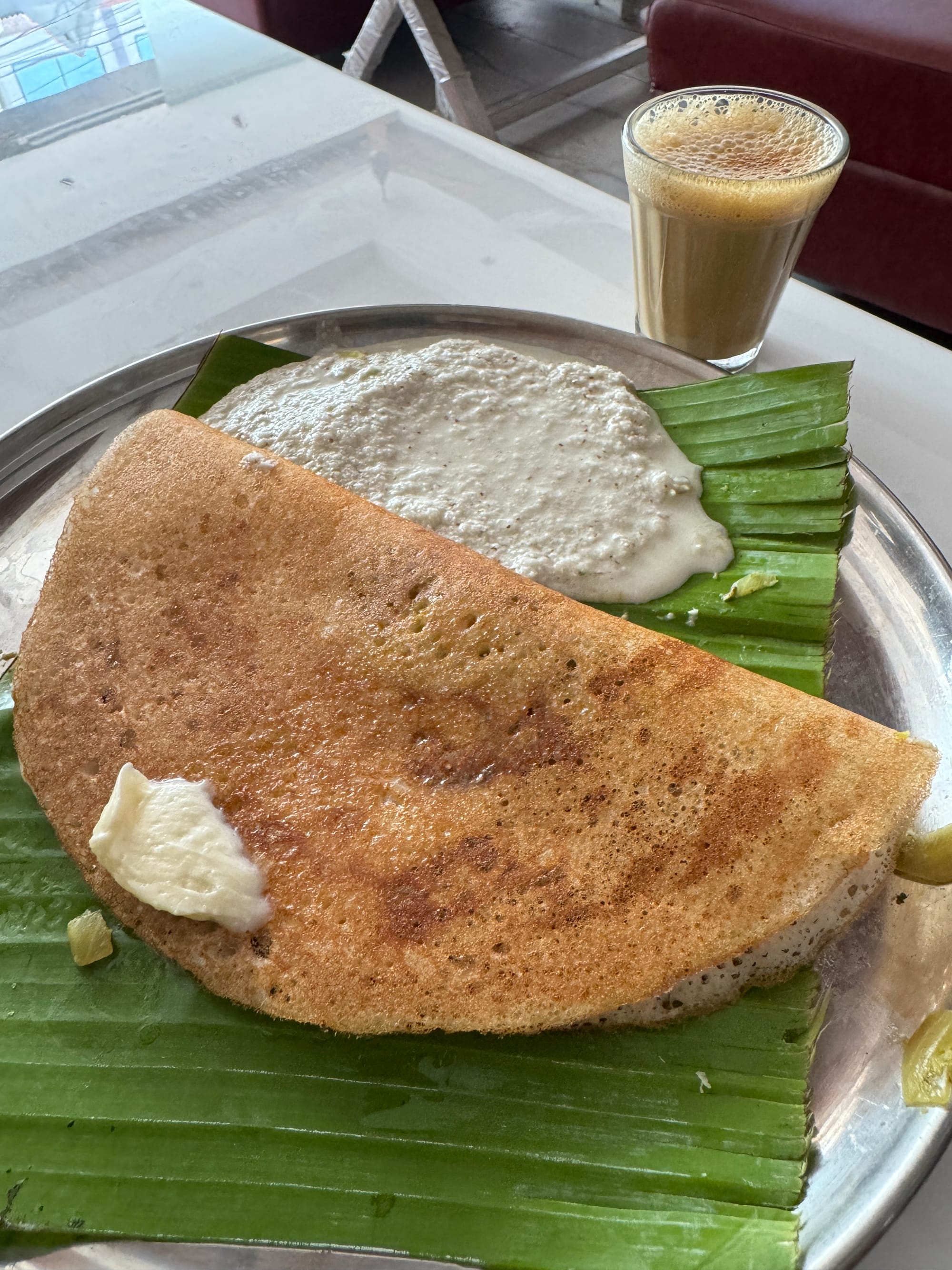 A folded dosa with ghee and coconut chutney on a banana leaf.