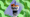 A Yankees branded plastic soda cup with a bowl on top of it filled with chicken tenders and fries, over a green and purple patterned background